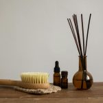 Minimalist aromatherapy set with essential oils, brush, and diffuser sticks on wooden table.