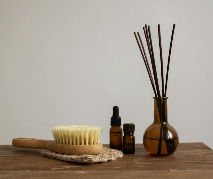 Minimalist aromatherapy set with essential oils, brush, and diffuser sticks on wooden table.